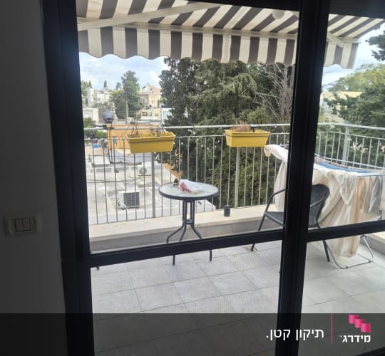 מבט מתוך דירה אל מרפסת שמש דרך דלת הזזה ומסך רשת
